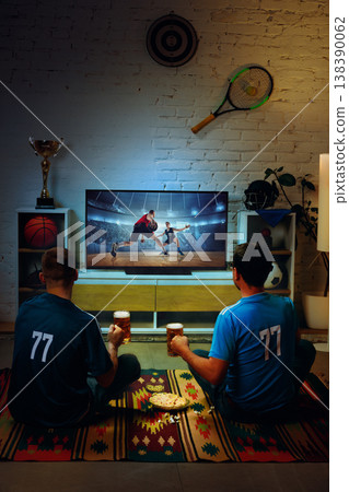 Two men watching basketball game on TV at home with beer and snacks. Two men watching basketball game on TV at home with beer and snacks. 138390062