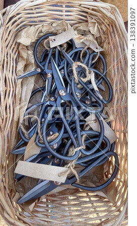 Heap of traditional forged steel garden shears with craft tags in a rustic wicker basket on display Heap of traditional forged steel garden shears with craft tags in a rustic wicker basket on display 138391097