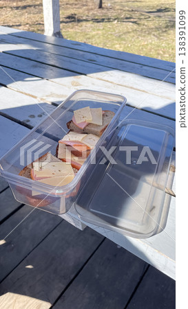 Plastic lunch box with fresh ham and cheese sandwiches on a rustic wooden table during a spring picnic Plastic lunch box with fresh ham and cheese sandwiches on a rustic wooden table during a spring picnic 138391099