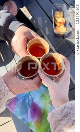 Top view of three people clinking paper cups with tea in a toast during a sunny spring outdoor picnic Top view of three people clinking paper cups with tea in a toast during a sunny spring outdoor picnic 138391108