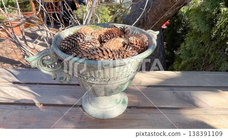 Vintage stone urn filled with natural pine cones on a wooden table in a sunny spring garden scene 138391109