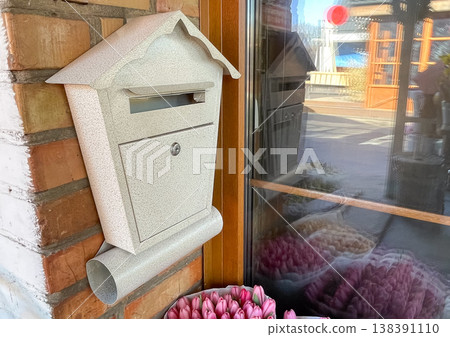 Vintage white mailbox on a red brick wall next to fresh pink tulips by a flower shop window display Vintage white mailbox on a red brick wall next to fresh pink tulips by a flower shop window display 138391110