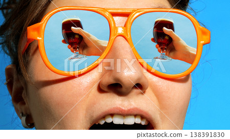 Woman in orange sunglasses with dark beer reflected in lenses under blue sky. Woman in orange sunglasses with dark beer reflected in lenses under blue sky. 138391830