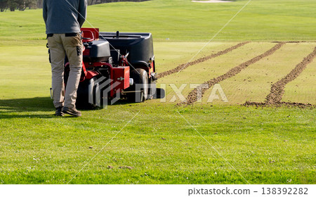 Groundskeeper aerating golf course green with professional turf maintenance machine on sunny day sports field care concept 138392282