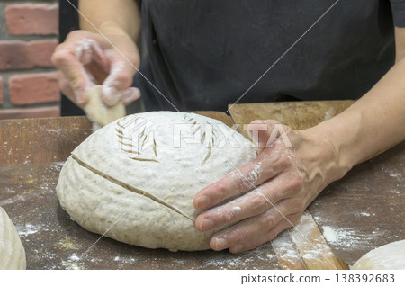 麵包師傅的手正在切開從發酵籃（藤籃）中取出的鄉村麵包麵團。 138392683