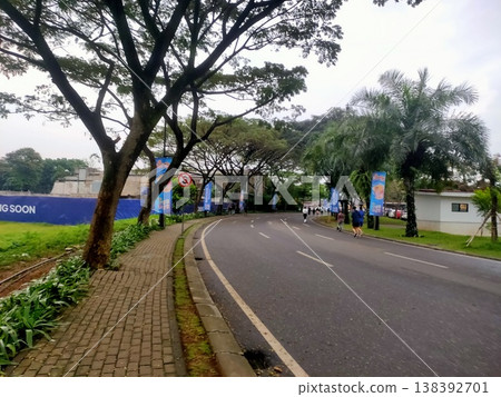 Curved tree-lined road with morning joggers and palm trees, creating a peaceful urban nature scene. Curved tree-lined road with morning joggers and palm trees, creating a peaceful urban nature scene. 138392701