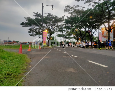 Evening crowd gathers on a lively street lined with trees, shops, and warm glowing streetlights. Evening crowd gathers on a lively street lined with trees, shops, and warm glowing streetlights. 138392735