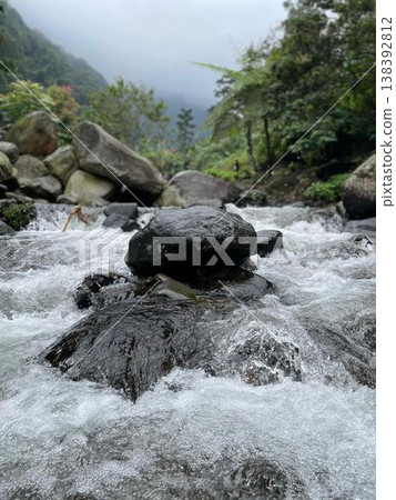 Crystal-clear river flowing over smooth rocks, framed by lush forest and misty mountain views. Crystal-clear river flowing over smooth rocks, framed by lush forest and misty mountain views. 138392812