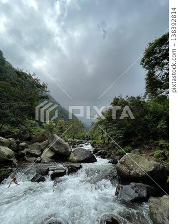 Crystal-clear river flowing over smooth rocks, framed by lush forest and misty mountain views. 138392814