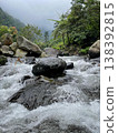 Crystal-clear river flowing over smooth rocks, framed by lush forest and misty mountain views. 138392815