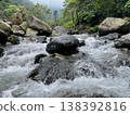 Crystal-clear river flowing over smooth rocks, framed by lush forest and misty mountain views. 138392816