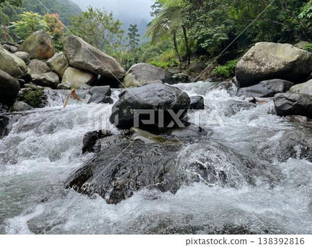 Crystal-clear river flowing over smooth rocks, framed by lush forest and misty mountain views. 138392816