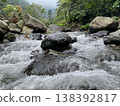 Crystal-clear river flowing over smooth rocks, framed by lush forest and misty mountain views. 138392817