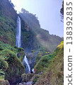 Tall waterfall cascading down lush green cliffs under sunlight, creating a serene and majestic view. 138392835