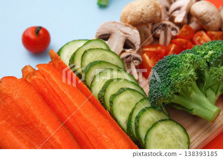 Healthy food background. Cut raw vegetables on wooden board. Chopped and sliced ingredients for salad or soup - mushroom, cherry tomato, broccoli, cucumber, carrot on bright background Healthy food background. Cut raw vegetables on wooden board. Chopped and sliced ingredients for salad or soup - mushroom, cherry tomato, broccoli, cucumber, carrot on bright background 138393185