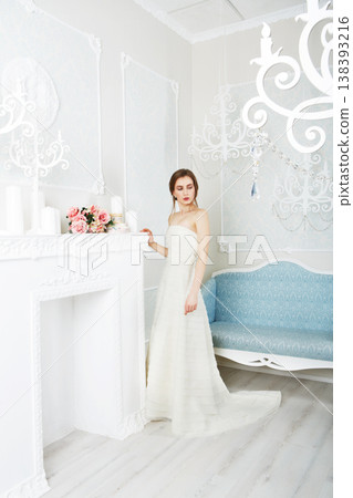 Wedding dress fashion. Beautiful young bride in vintage wedding dress indoors. White wedding dress at model. Girl shows wedding fashion in decorated shabby chic interior with flowers, high key. Wedding dress fashion. Beautiful young bride in vintage wedding dress indoors. White wedding dress at model. Girl shows wedding fashion in decorated shabby chic interior with flowers, high key. 138393216