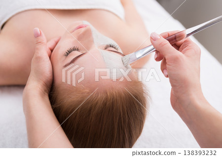 Apply face mask, spa beauty treatment and skincare. Woman getting facial nourishing mask by beautician at spa salon, close-up Apply face mask, spa beauty treatment and skincare. Woman getting facial nourishing mask by beautician at spa salon, close-up 138393232