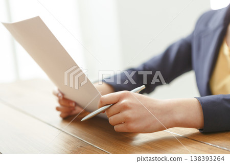 Female reading documents while sitting at wooden table, close-up, side view. 138393264
