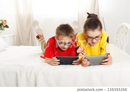 Two children, siblings on parents bed at morning with laptop and tablet. Brother and sister play computer games. Siblings and gadgets. Children with pet, chiwawa dog in bed. Children in glasses. Two children, siblings on parents bed at morning with laptop and tablet. Brother and sister play computer games. Siblings and gadgets. Children with pet, chiwawa dog in bed. Children in glasses. 138393268