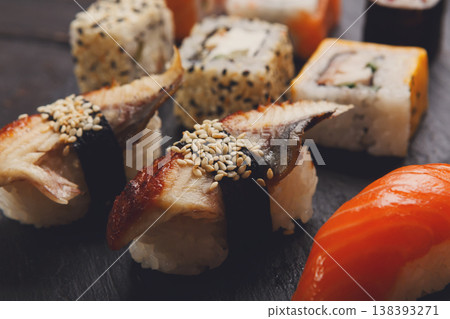 Sushi and rolls closeup. Japanese restaurant delivery. Salmon, unagi, california and other healthy meals on dark wooden background Sushi and rolls closeup. Japanese restaurant delivery. Salmon, unagi, california and other healthy meals on dark wooden background 138393271