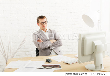 Young businessman working in white modern office interior, smiling, sitting at computer table. Office worker in eye glasses, male, job in internet. High key, soft tone. Business man in modern office. 138393272