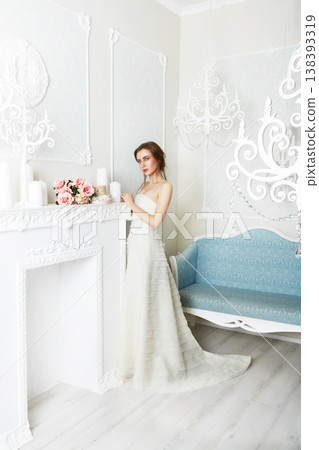 Wedding dress fashion. Beautiful young bride in vintage wedding dress indoors. White wedding dress at model. Girl shows wedding fashion in decorated shabby chic interior with flowers, high key. Wedding dress fashion. Beautiful young bride in vintage wedding dress indoors. White wedding dress at model. Girl shows wedding fashion in decorated shabby chic interior with flowers, high key. 138393319