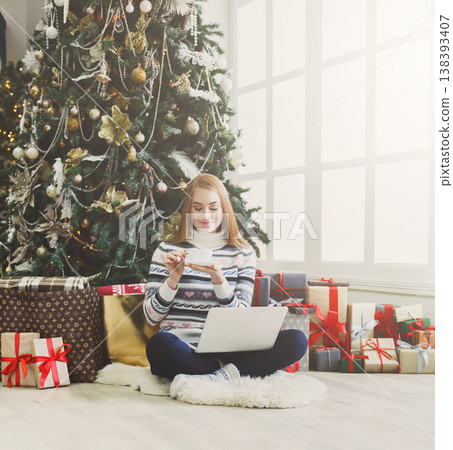 Christmas online shopping. Woman has coffee, buy presents on laptop, prepare to xmas, among gift boxes and packages. Winter sales Christmas online shopping. Woman has coffee, buy presents on laptop, prepare to xmas, among gift boxes and packages. Winter sales 138393407