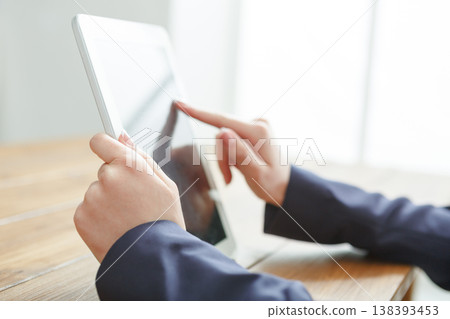 Woman using digital tablet while sitting at wooden table, close-up, side view. Woman using digital tablet while sitting at wooden table, close-up, side view. 138393453