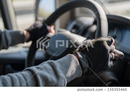 Driver hands on steering wheel wearing gloves inside car interior close up safe driving transportation concept Driver hands on steering wheel wearing gloves inside car interior close up safe driving transportation concept 138393460