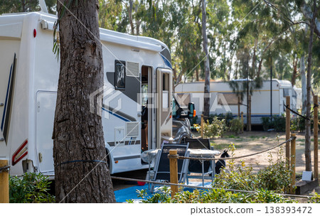 Motorhome parked at campsite with outdoor chairs and forest surroundings summer travel camping vacation lifestyle concept Motorhome parked at campsite with outdoor chairs and forest surroundings summer travel camping vacation lifestyle concept 138393472