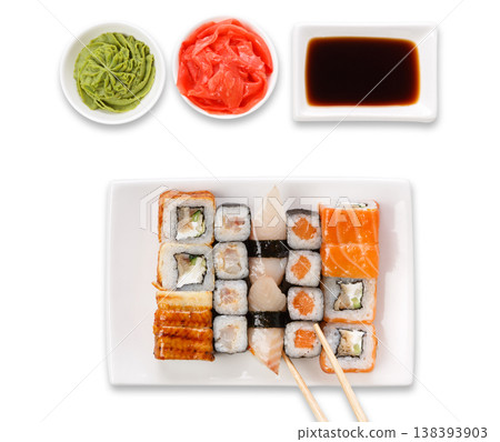 Japanese food restaurant. Sushi set served on white platter with soy sauce, ginger, wasabi and chopsticks picking one piece. Top view, flat lay at white background with copy space 138393903