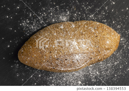 a fresh soft loaf of bread on black slate, a baked soft loaf of rye bread lies on the table a fresh soft loaf of bread on black slate, a baked soft loaf of rye bread lies on the table 138394553