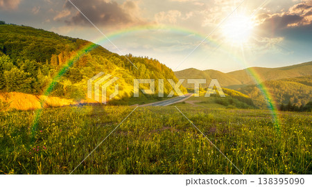 sunset over mountainous rural landscape in summertime. picturesque highland woods and grassy meadow. view of countryside scenery with forested hills behind the pasture under rainbow sunset over mountainous rural landscape in summertime. picturesque highland woods and grassy meadow. view of countryside scenery with forested hills behind the pasture under rainbow 138395090