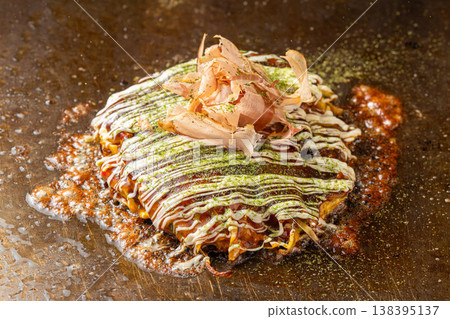 大阪燒:一種在鐵板上烹調的受歡迎的大阪燒菜餚,散發著醬汁的香味。 大阪燒:一種在鐵板上烹調的受歡迎的大阪燒菜餚,散發著醬汁的香味。 138395137
