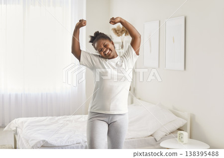 Joyful African American woman standing and stretching in her bedroom after waking up in morning. Joyful African American woman standing and stretching in her bedroom after waking up in morning. 138395488