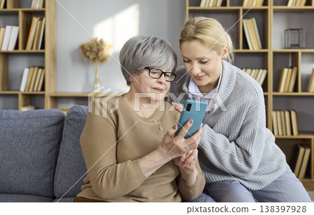 Younger woman teaching senior to use smartphone at home, tech help and support Younger woman teaching senior to use smartphone at home, tech help and support 138397928