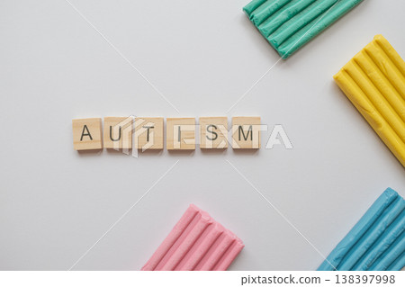Minimalist composition featuring the word AUTISM in wooden tiles alongside vibrant modeling clay. A symbolic visual for neurodiversity and sensory awareness on a clean background 138397998