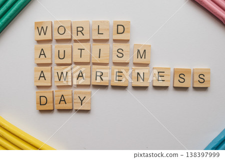 Top-view photo of WORLD AUTISM AWARENESS DAY in wooden tiles on a white background. Vibrant clay accents symbolize the spectrum, offering clean copy space for design 138397999