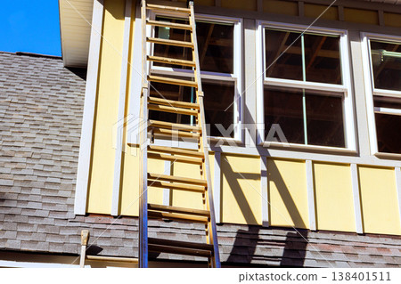 Ladder stands against yellow primed smooth fiber siding by windows, ready for installing work fiber siding Ladder stands against yellow primed smooth fiber siding by windows, ready for installing work fiber siding 138401511