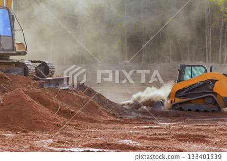 Heavy machinery clears land in construction zone as dust dirt fill air in forest setting. 138401539