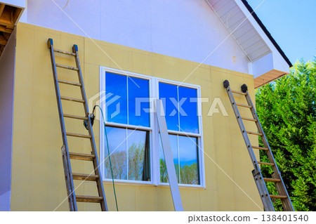 Ladders are leaned against side of house as workers plan to paint exterior after installing fiber siding Ladders are leaned against side of house as workers plan to paint exterior after installing fiber siding 138401540