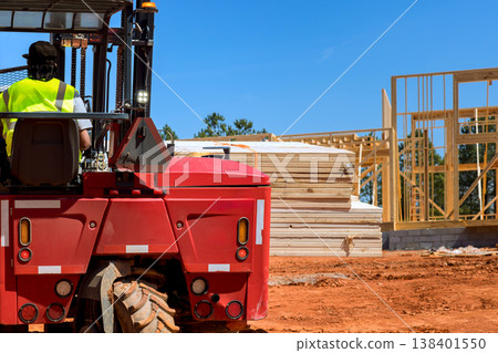 Forklift operator moves stacks of lumber on construction site where workers build new structures outside. 138401550