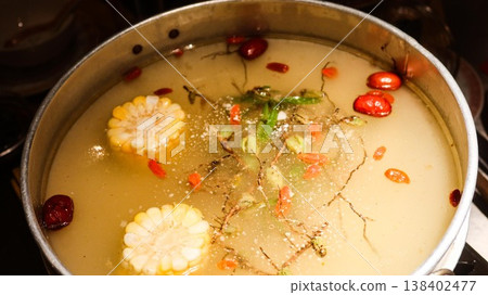 close up of a Chinese hot pot with boiling soup with corn, red dates, herbs, greens, Cordyceps Flower and chicken with chopsticks and large spoon close up of a Chinese hot pot with boiling soup with corn, red dates, herbs, greens, Cordyceps Flower and chicken with chopsticks and large spoon 138402477