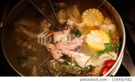 close up of a Chinese hot pot with boiling soup with corn, red dates, herbs, greens, Cordyceps Flower and chicken with chopsticks and large spoon close up of a Chinese hot pot with boiling soup with corn, red dates, herbs, greens, Cordyceps Flower and chicken with chopsticks and large spoon 138402482