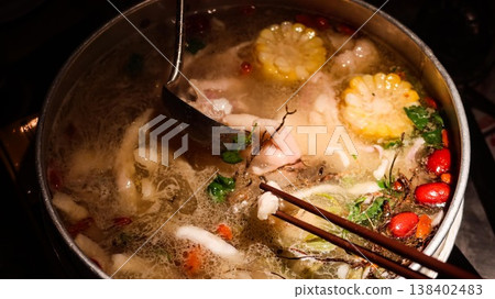 close up of a Chinese hot pot with boiling soup with corn, red dates, herbs, greens, Cordyceps Flower and chicken with chopsticks and large spoon close up of a Chinese hot pot with boiling soup with corn, red dates, herbs, greens, Cordyceps Flower and chicken with chopsticks and large spoon 138402483