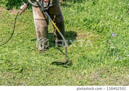Man trims grass with an electric trimmer in dirty clothes at his house Man trims grass with an electric trimmer in dirty clothes at his house 138402502