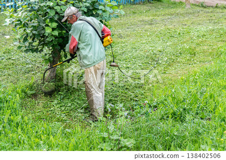 Elderly man mows grass with electric trimmer in front of his home Elderly man mows grass with electric trimmer in front of his home 138402506