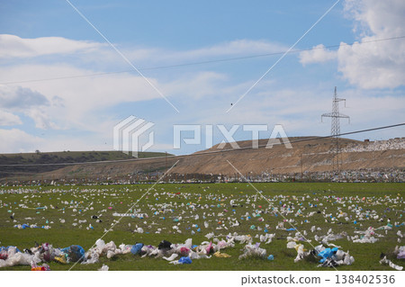 Wide shot of colorful plastic bags littering a green field near a large industrial landfill 138402536