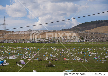 Wide shot of colorful plastic bags littering a green field near a large industrial landfill 138402537