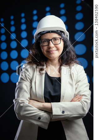 Woman engineer wearing hard hat smiling confidently with arms crossed 138402590